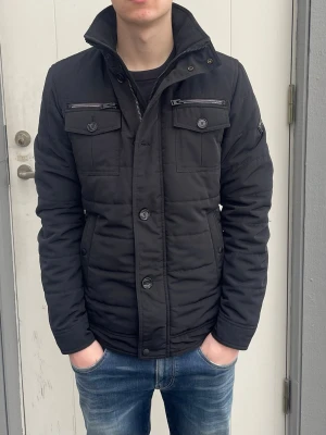 Svart Fieldjacka från J.lindeberg - S - Jag säljer den här riktigt snygga fieldjackan från J.lindeberg i storlek S. Den är inte använd mycket alls och är i fint skick utan skador och defekter. Modellen heter Bailey 56 Structured Poly. Nypris på en sån här låg på 3400kr och jag säljer den för 1499kr. Tveka inte att höra av er!