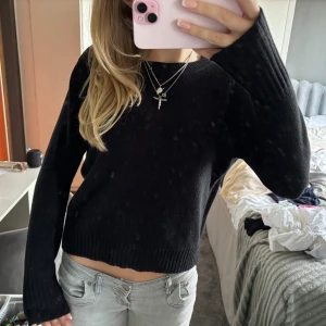 Svart stickad tröja - En svart stickad tröja med långa ärmar och ribbstickade muddar vid ärmslut och nederkant. Tröjan har en normal passform och är bekväm för vardagsbruk.