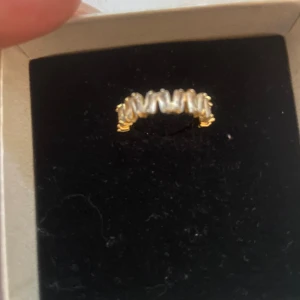 Guldfärgad ring med pärlor - En elegant guldfärgad ring dekorerad zirkonstenar. Ringen har en unik design med zirkonstenar placerade i en rad längs med ringen.