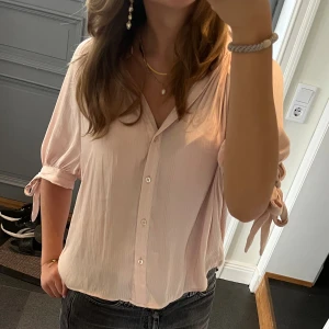 Rosa kortärmad blus  - Rosa/beige kortärmad blus med snörning från H&M i storlek 38. Passar S och M. Fint skick. Använd gärna köp nu!