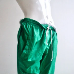 Retro trackpants - Retro trackpants i glansigt grönt tyg med innertyg i mesh. Kan öppnas från ankeln en bit upp på vaden med dragkedjor. Stora fickor, dragsko i midjan. 
