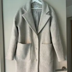 Lång kappa i ull från NA-KD, använd 5 gånger. I storlek 38. En grå, beige färg 