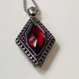 Vackert halsband med rubinröd sten på kedja  Kedjan är ca 90 cm och hänget 7 cm inklusive ögla   Okänt material 