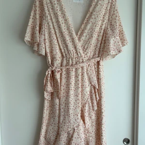 Blommig klänning Sisters point Strl L - Supersöt blommig klänning med resår i midjan, klänningen har en wrap klännings effekt men sitter helt ihop, har ett löst band i midjan. Använd någon enstaka gång, som nyskick! Storlek L 