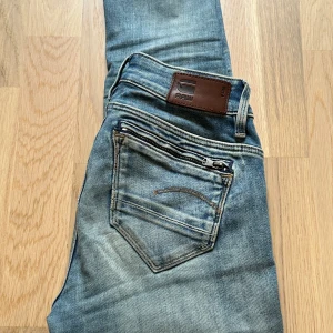 G-STAR RAW, MIDGE ZIP MID SKINNY - Jeans Skinny Fit - Dessa Mid Wasted G-STAR jeans har två hål i sig och har dragkedjor på  bakfickorna. De har burits ett par gånger.  Priest går att diskutera! Storlek: Width - 24  Length - 30