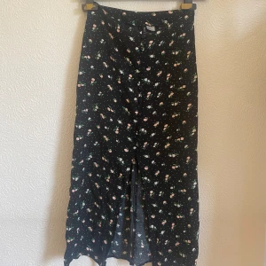 Midikjol - Svart midikjol med blommigt mönster från H&M i storlek 32. Den har fina knappar där fram som detaljer och har även en slits. Den är använd men i fint skick
