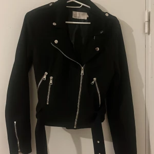 Svart vår jacka  - Svart vår jacka i mocka material. Har silver detaljer och är i väldigt bra skick. Fungerar att ha under vår eller höst och är relativt kort. Köpt från Nelly i storlek 36.