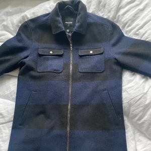 Vårjacka - Only & Sons - En tunnare jacka perfekt för våren från Only & Sons. Mörkblå och svart rutmönster gör att det passar till det mesta! En herrjacka i storlek M. Inte använt på ett bra tag så dags att sälja den vidare! I väldigt bra skick inga flaws eller fläckar!:)