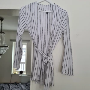 Svartvit randig kavaj/blazer/kofta - En snygg tunn blazer, knyt i midjan eller ha den öppen. Klär lätt upp en bas outfit. Endast använd några gånger, normal i storlek. Kom med prisförslag 😊  Material: 95% Polyester, 5% Elastan.