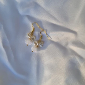 White Snow Petal Earrings - Fina örhängen med guldfärgad metall och fina vita pärlor. Ploppar ingår.  Alla beställningar från oss kommer fint paketerade 🤍