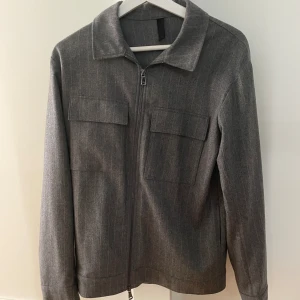 J.Lindberg - Säljer en stilig grå overshirt i storlek Medium. Den är i mycket gott skick och passar perfekt för lager-på-lager stil eller som en lätt jacka. 