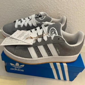 Nya Adidas Campus 00s -storlek 38 - Adidas Originals Campus 00 s j stö: 38 Färg: Grå (Grey Three / Cloud White / Cloud White) Ingår både vita och gråa skosnören.  Nya och oanvända. Ligger kvar i kartong.  Köpta i Sverige och inte från massbeställning utomlands. 100% äkta. 