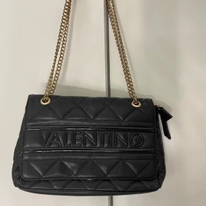 Valentino väska  - En snygg svart valentinoväska. Kan bäras både över kroppen och över axeln. Tappat en del färg på kedjan.