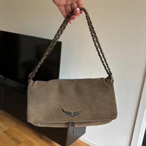 Zadig väska - Väska från Zadig & Voltaire i brun/mörk beige mocka, modellen Rock. Bra begagnat skick! Både det långa och korta bandet medkommer. Givetvis äkta. 