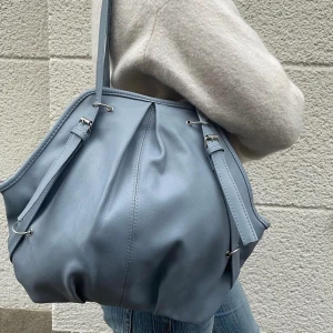 Handväska - Säljer denna söta handväska i en blå/grå färg. Den är sparsamt använd och i ett gott skick! Den har dock hängt ett tag så sömmarna har släppt lite från en del av bandet. Väldigt lätt att fixa men inget som syns. Lånade bilder, pris kan diskuteras! 