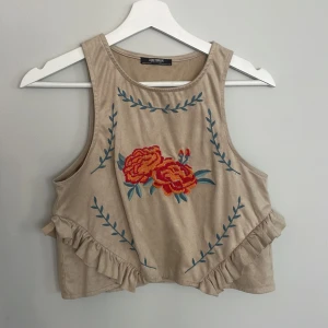 Zara kort linne halterneck med broderadi & volang - Kort linne / magtröja med lite halterneck stil från Zara.  Materialet känns som mocka (men är inte äkta)  Fint broderi och volang, perfekt för vår och sommar!