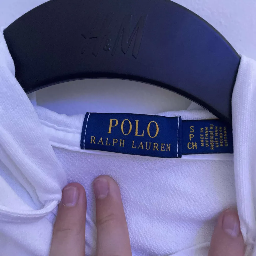 En vit huvjacka från Polo Ralph Lauren med dragkedja framtill och två fickor. Jackan har en broderad logotyp på bröstet och en huva med dragsko.. Jackor.