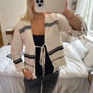 zara trekvartsärmad kofta med fransar - trekvartsärmad beige/vit kofta från zara med fransar. svarta broderade detaljer och tunt material! storlek XS men passar XS-M. skriv för fler bilder!