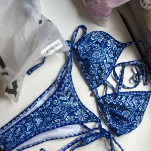 Blå och rosa bikinis - Två olika bikinis till salu. Den första är en blå bikini med ett blommigt mönster och snörning. Den andra är en rosa bikini med glittriga detaljer och knytband. Båda är självklart OANVÄNDA!! gillade inte mönstret när jag fick hem dom.