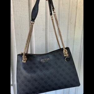 Guess väska  - Säljer nu min guess väska, inköpt för 2 månader sedan, använd några få tillfällen, köpte för 1769 kr ny, säljer för 1300! Något vitt märke nere som knappt syns då det är på gränsen till undersidan, annars superfin och rymlig väska! 