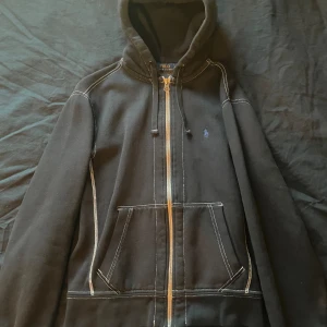Svart jacka från Polo Ralph Lauren - En svart jacka från Polo Ralph Lauren med dragkedja och huva. Jackan har vita sömmar och två framfickor. 10/10 condition never worn
