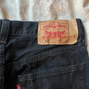 Svarta jeans från Levi's - Ett par svarta jeans från Levi's i modell 501. Jeansen har en klassisk design med fem fickor och knappgylf. De är i storlek 31 L 32 och har en rak passform.
