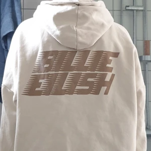 Beige hoodie med tryck - En beige hoodie med tryck från Billie Eilish. Hoodien har en stor logotyp på ryggen och ett mindre tryck på framsidan. Den har långa ärmar och en justerbar huva med dragsko. Köpt på H&M. Storlek S. Inte använd sen 2023💓
