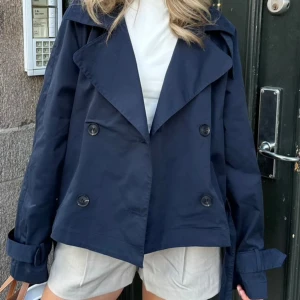 Kort trenchcoat  - Säljer denna supersnygga marinblåa korta trenchcoaten från BY IC då den inte kommer till användning.  Aldrig använd!   (Bilderna är från BY IC hemsida, skriv för fler bilder) 