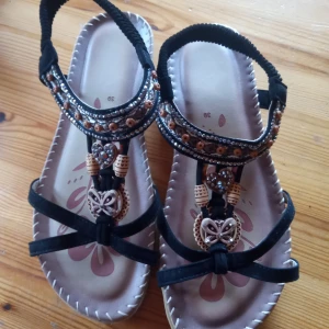 Sandaler med pärlor i olika färger . - Fina och tuffa Sandaler med pärlor i olika färger och töjbar vristrem .storlek 39. Mycket fint skick .hämtas i Skene alt skickas .