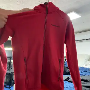 En röd hoodie från Peak performance i storlek L. Tröjan är i fint skick, har dock en fläck på armen(se bild) som tyvärr inte går bort. I övrigt super fin men kommer tyvärr inte till användning! Köparen står för frakten! 