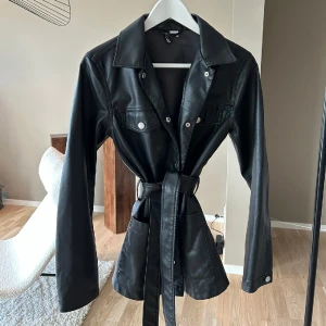 Jacka med knyt - Säljer denna superfina jacka med knyt i läderimitation från divided då den inte kommer till användning. Jackan är i nyskick