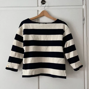 Randig tröja - En vit- och blårandig tröja köpt på Lindex. Tröjan är kort i ärmarna och har guldknappar längst ner. Storleken är XS. Använts få gånger 😊