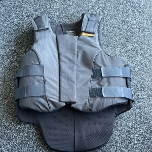 RIDVÄST, SOM NY - jag säljer en ridväst som är använd 2 gånger, tills jag inte hade någon användning för den. En svart ridväst med orangea detaljer/band. Storlek L 3 Reg.  Nypris: 3100, säljer för: 2400