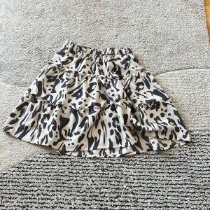 Kjol - Den är 45 cm lång och 29 cm bred. En kjol med svart och ljus beiga färger. Den är i jätte jätte bra skick. Den är gjord av polyester och elastan. 