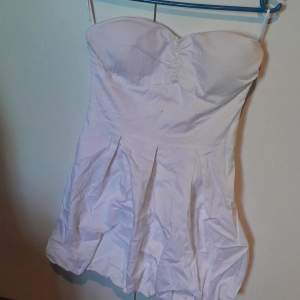 En vit puffig ballongklänning utan ärmar. Dragkedja finns på vänster sida.