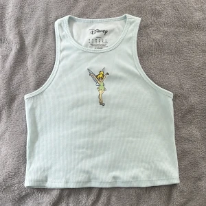 Croptop Tingeling - Supersöt ljusblå croptop med Tingeling broderat på framsidan. Användes en gång på en temafest för tidigt 2000-tal😂 gullig och väldigt skönt material! Står M som storlek men passar nog XS och S också