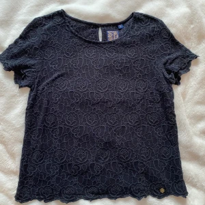 Svart topp med blommigt spetsmönster i strl M från Superdry - Svart topp med blommigt spetsmönster i strl M från Superdry.  Sparsamt använd och i fint begagnat skick.  Mått Över bröstet: ca 49 cm Längd från axeln och ner: ca 60 cm  100% viskos  Kommer från ett djur och rökfritt hem. 