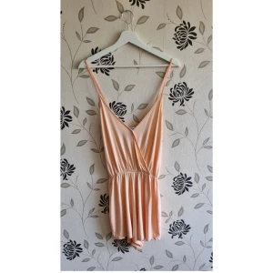 NLY Trend, wrap playsuit, Strl: XS/34, "Peach" Persika, sommar, summer, nyskick - Nly Trend playsuit i storlek XS/34 - nyskick!  "Playsuit från NLY Trend. V-ringad design med tunna axelband. Elastisk midja och stretchigt material."  OBS! Jag kan inte skicka något vecka 26.