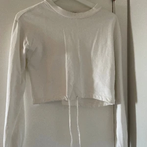 Vit croppad topp med knytning  - Croppad långärmad tröja med knytning i midjan. Från Nelly 