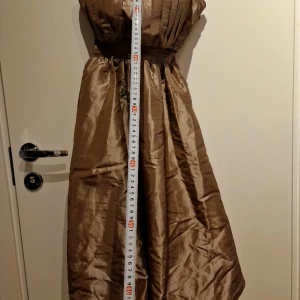 Vila klänning stl XS - Vila klänning stl XS  Använd en gång Öppnar med dragkedja på sidan, har lite stretch bak och midja  Man kan ha klänningen med eller utan axelband.  Lite svårt att säga exakt färg, men en blandning av brun, brons (grön?)