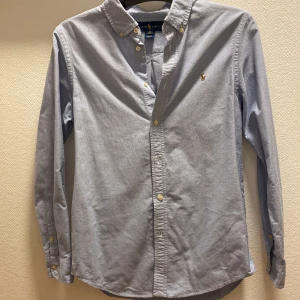 Ralph Lauren skjorta  - Fin ljusblå Ralph Lauren skjorta i storlek 18 Sitter som S-M Skick: 9/10, bara använd ett fåtal gånger. Skriv PM för fler bilder Kan lösa paketpris om man vill ha båda skjortorna på min sida :) Mvh