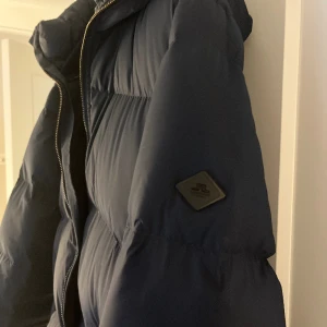 Herr dunjacka j.lindeberg  - Säljer en dunjacka i herrmodell från J.Lindeberg, nyskick och endast använd 2 gånger, marinblå med luva, har fler bilder vid intresse, den har bla. innerfickor. Köpt för 4500kr🥰