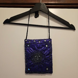 Handväska, festival, boheme - Beskrivning: Lila väska med pärldetaljer Märke:  Storlek:  Skick: Oanvänd  Material:   Nakenkatt finns i hemmet