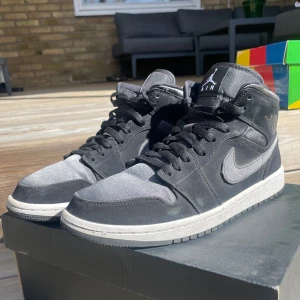Air Jordan 1 Mid - Air Jordan 1 mid, svarta och grå/silvriga. Inte använda så mycket men har skejtat i de ett fåtal gånger, därav några märken. De är dock creasade! 
