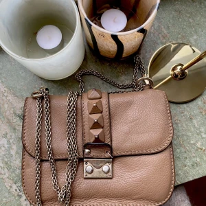 Valentino Rockstud Glam Lock bag - Säljer min otroligt fina Valentino Garavani väska. Inköpt på Vestiaire 2021 för 9000kr och är autentiserad därigenom.  Nitarna är lite slitna men det märks verkligen inte när man använder den. Eftersom den är i använt men gott skick har jag satt ett 