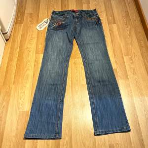 (25) Låga bootcut jeans helt nya med lappar kvar. Sjukt fina rhinestons och andra detaljer på fram och bakficka. Midjemått rakt över: 37 cm, innerbenslängd: 88cm 🩵