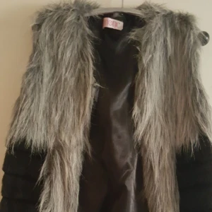 Originell pälsväst - Vintage pälsväst i ovanlig modell. Två sorters päls, beige lurvigt upptill och kanterna och svart slät, glansig i övrigt och  midja i bak. Mina bilder får ju aldrig plats men skickar gärna hela bilderna. (Gäller alla mina annonser.) Aldrig använd, i 