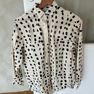 Skjorta - Utanpåskjorta i beige och svart. 100 % bomull. Längre baktill.