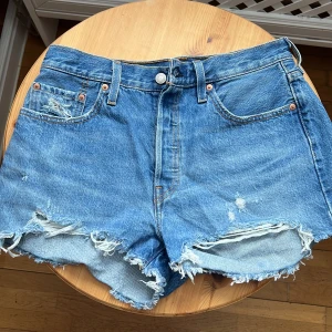 Levis-shorts - Levis 501 jeansshort i strl 29. Knappt använda, men har fransar och ”slitage” som var där när jag köpte dom i levisbutiken💛Tog en ny bild på dom i dagsljus då det känns som att dom är mer blå än grå irl!