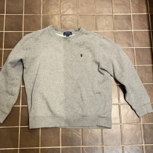 Grå Ralph Lauren sweatshirt (14-16). 400 kr - Säljer en grå Ralph Lauren sweatshirt med blått märke. Tröjan är storlek 14-16 år och säljs pga att den är för liten. Tröjan är i väldigt bra skick. Jag säljer tröjan för 400 kr